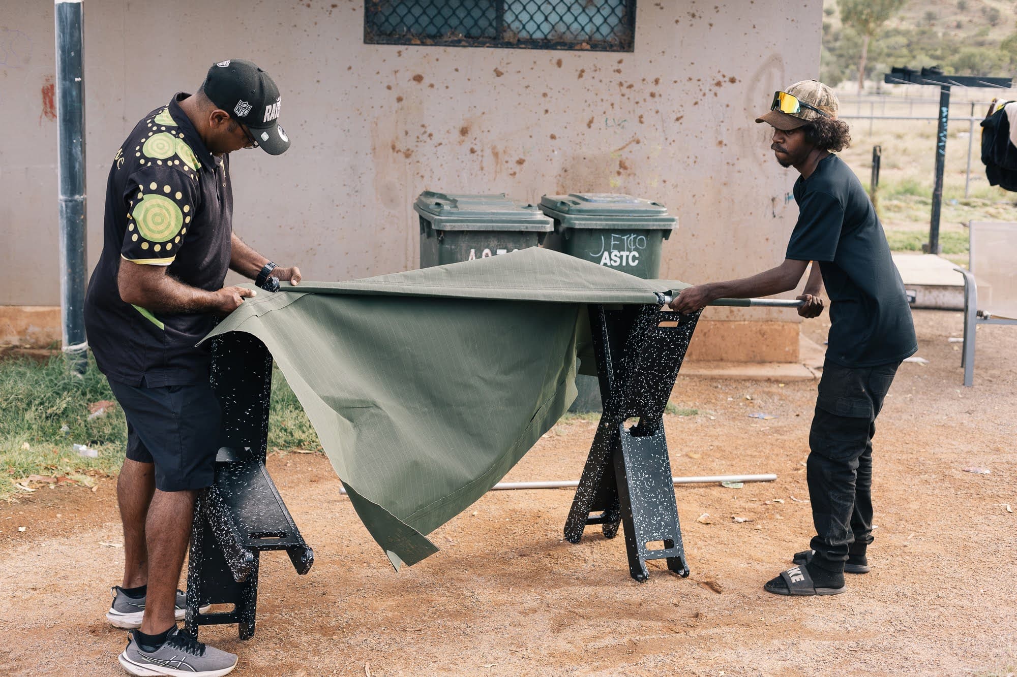 Two community members threading canvas over the bed frame