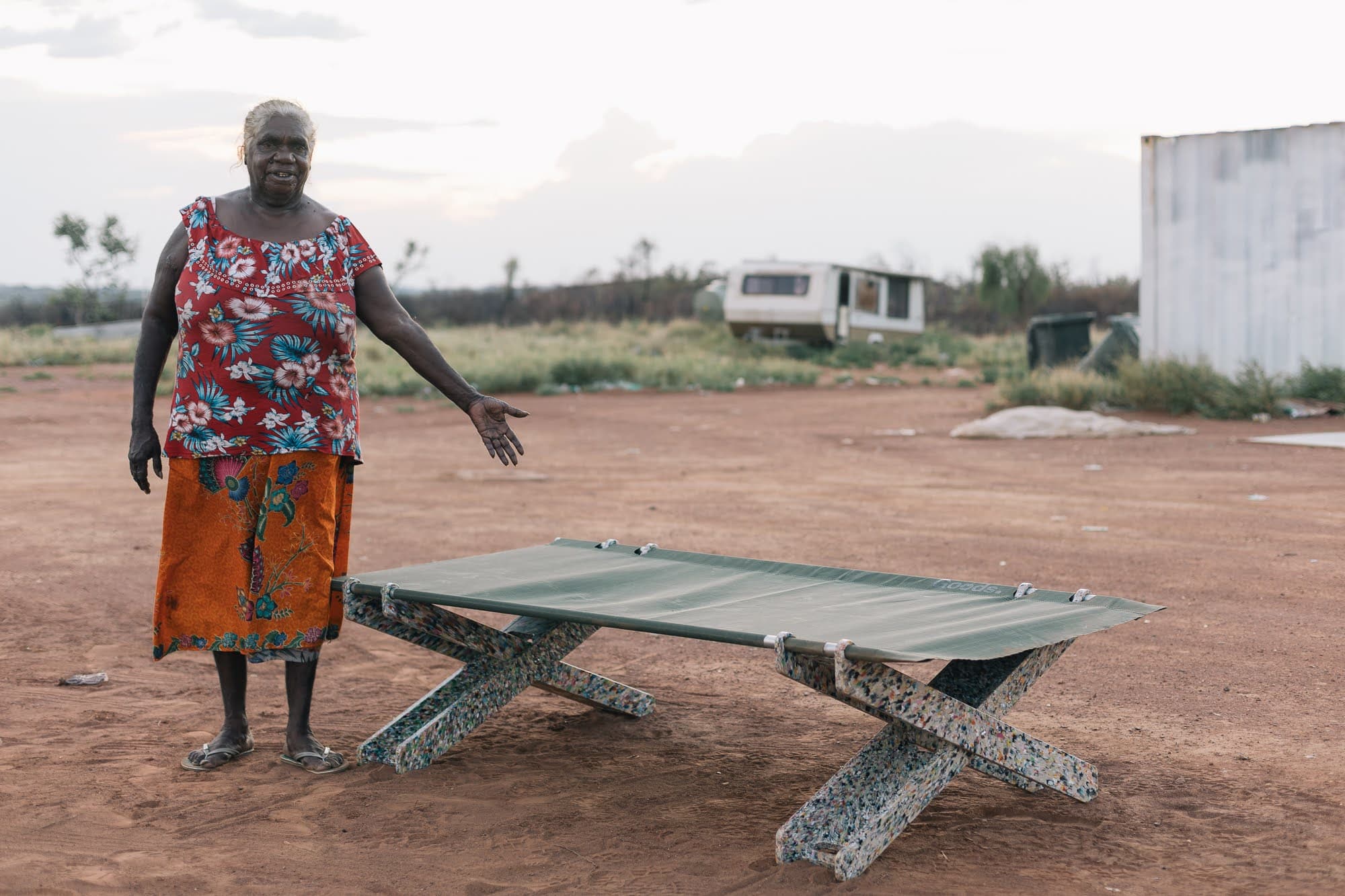 Elder woman standing proudly next to assembled Stretch Bed on red dirt